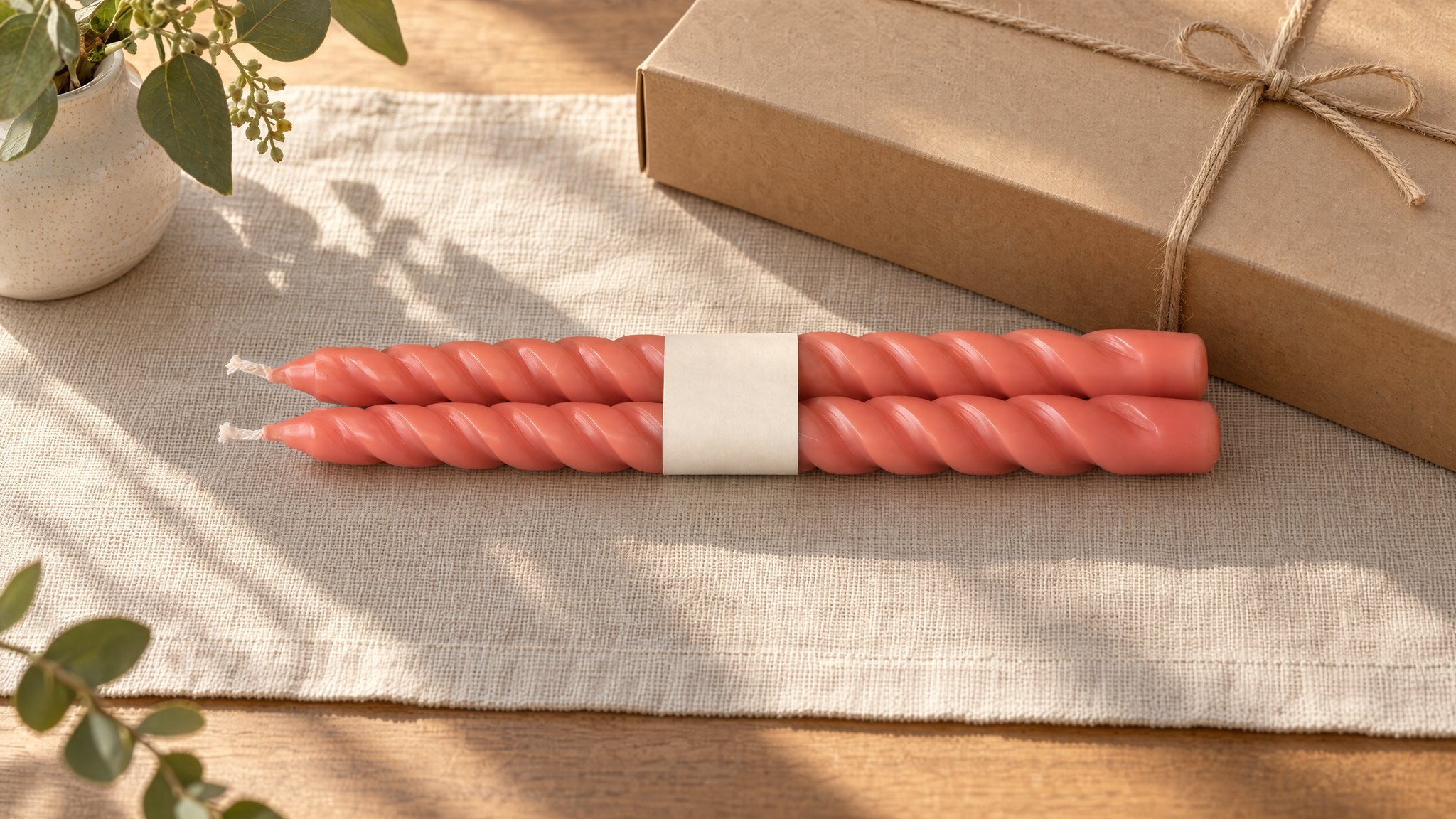 Velas coral en espiral sobre lino junto a una caja kraft