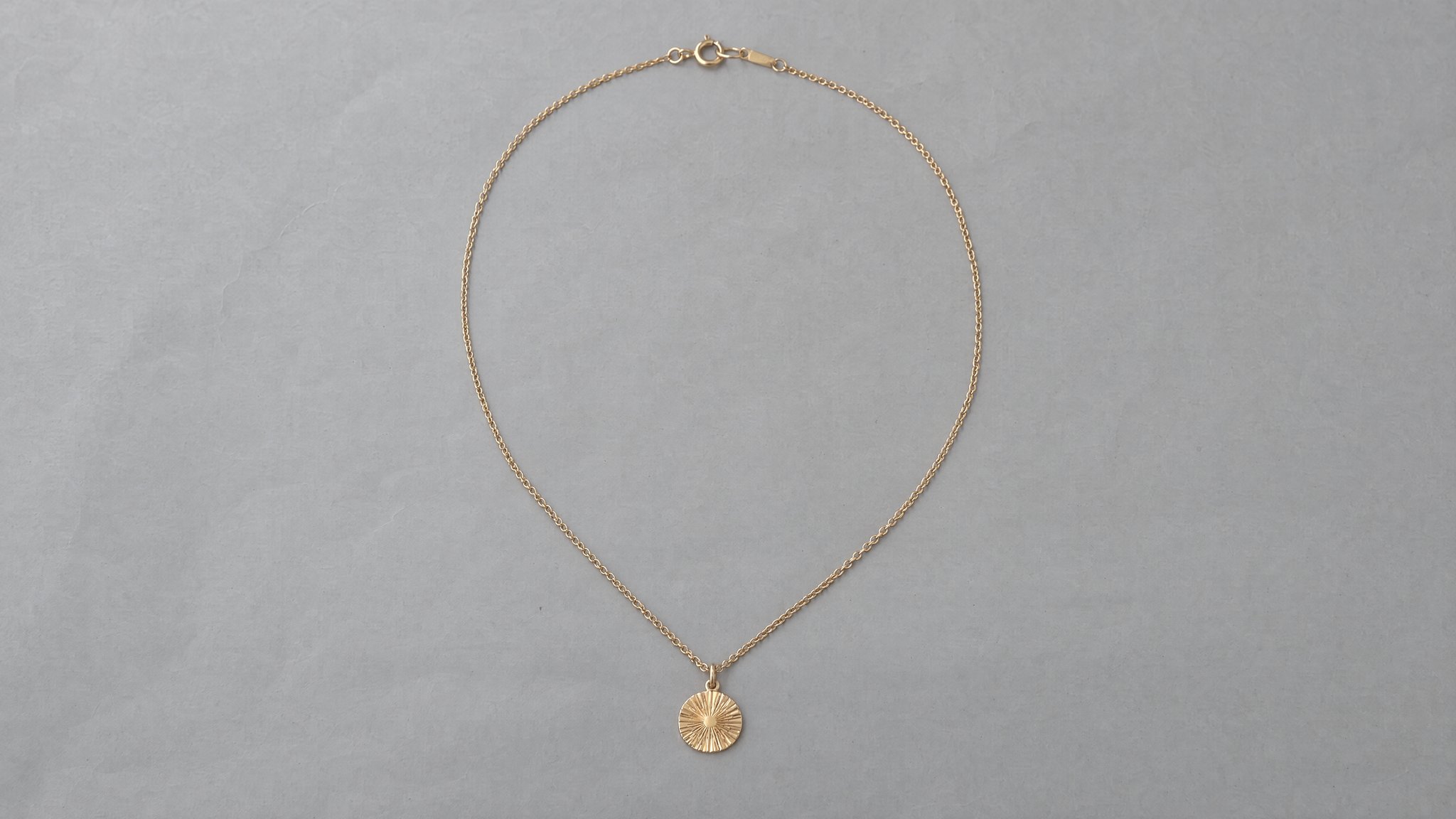 Collar de oro con medallón redondo y cierre visible sobre papel gris, generado con IA