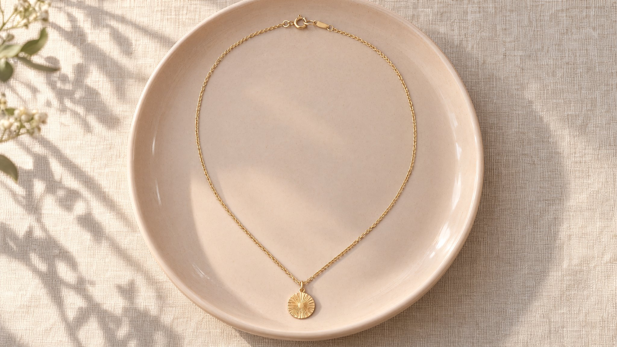 Collar con medallón de oro en un plato color melocotón sobre lino