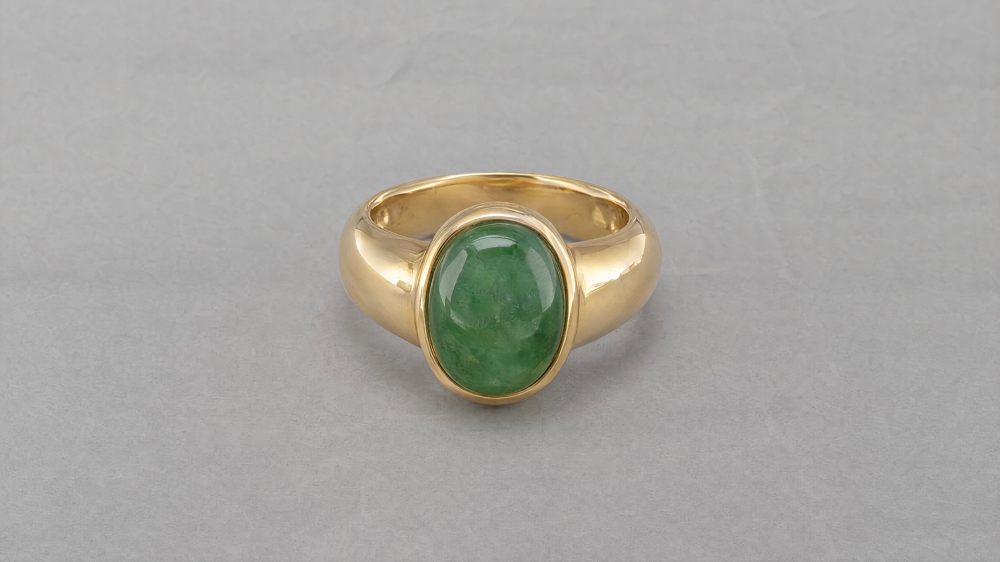 Anillo de oro con piedra ovalada verde sobre papel gris, generado con IA