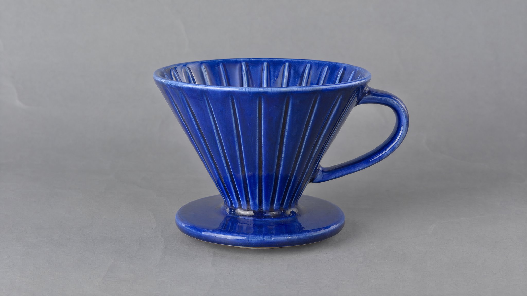 Blue ceramic coffee dripper on creased gray paper, generated with AI