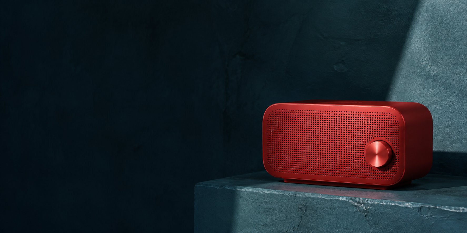 A red portable speaker on a dark teal stone ledge in directional studio light