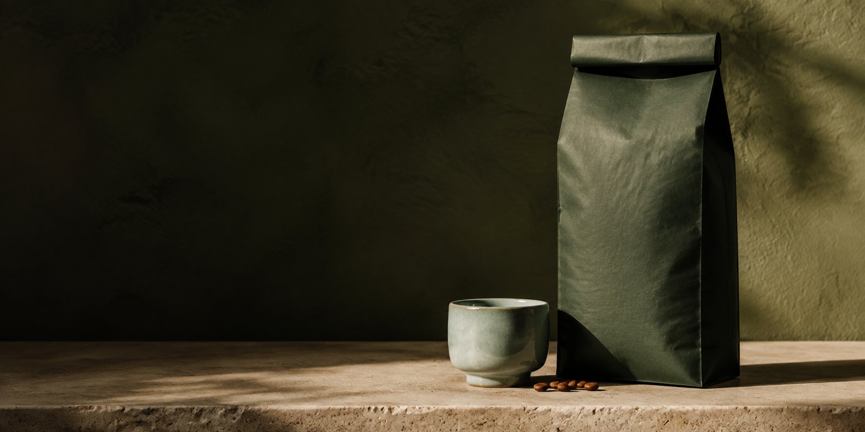 A forest-green coffee bag and sage espresso cup on limestone in a softly lit coffee roastery